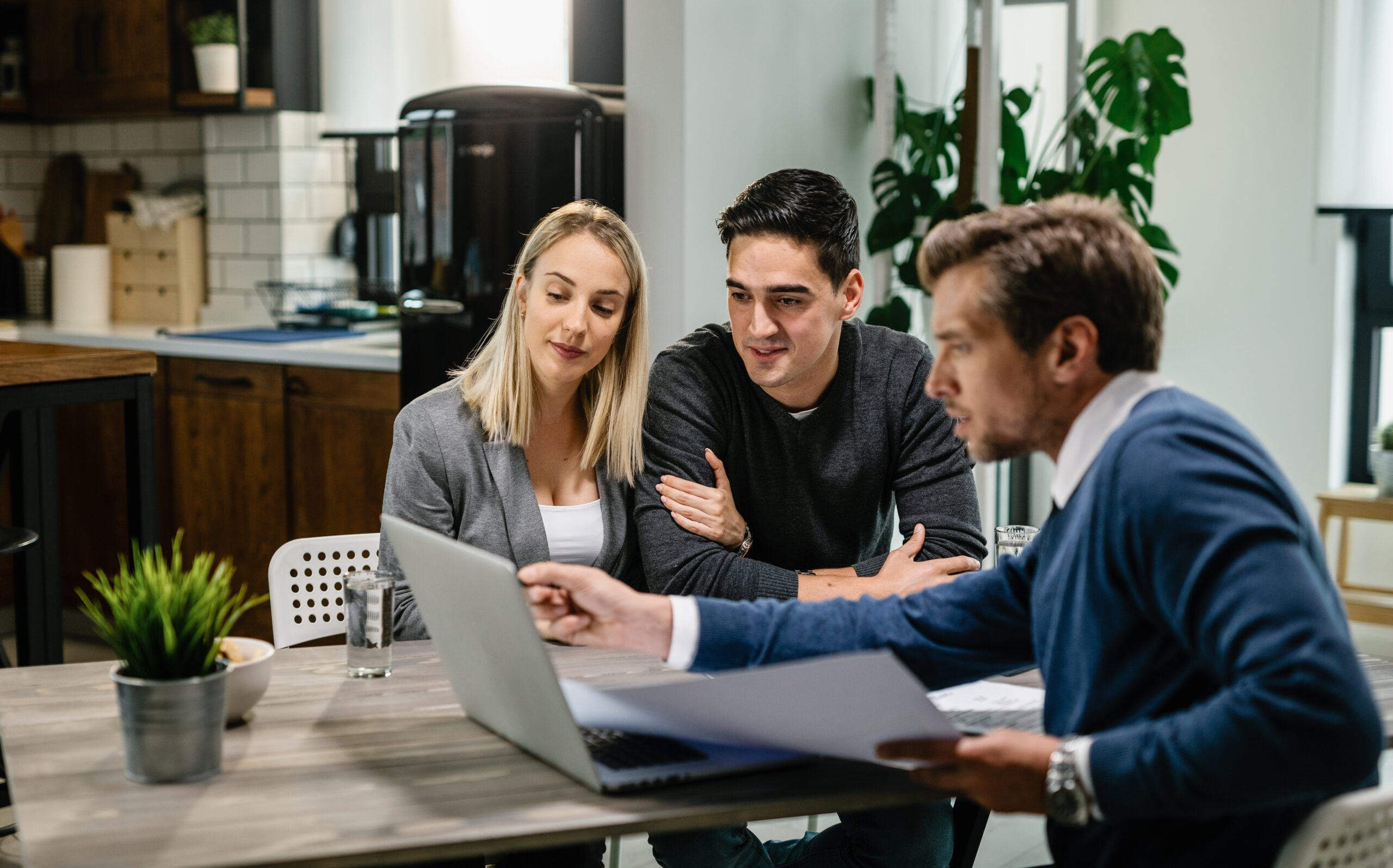 Young Couple Real Estate Agent Using Laptop While Going Through Housing Plan Meeting Scaled